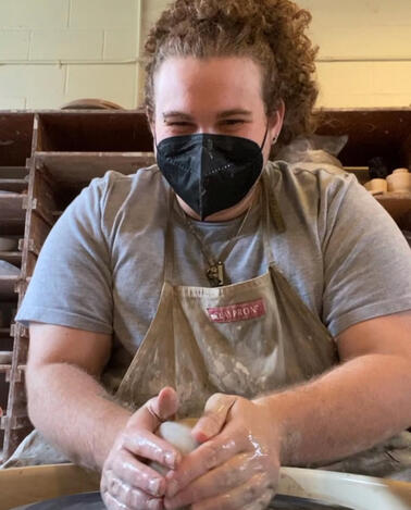 Nat Wood sitting at the pottery wheel smiling and throwing pottery.